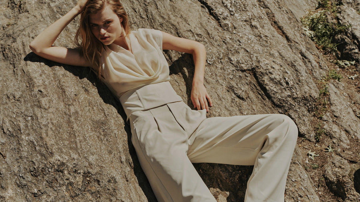 Bayse shipping and delivery: model in a cream top and trousers reclining on a rock